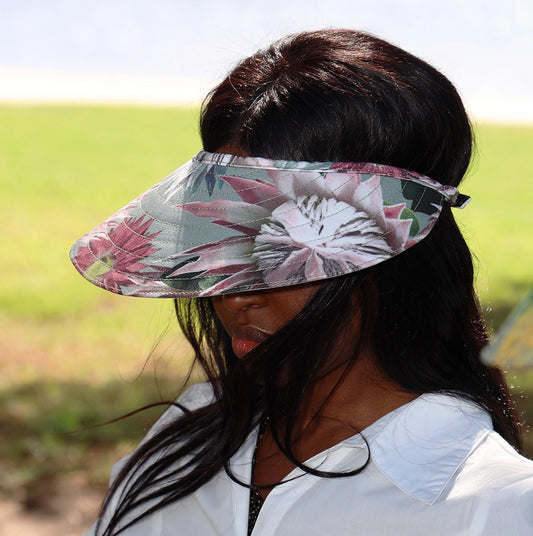 Girl wearing a Wild Things Floral sun visor with pink proteas on a soft green background.