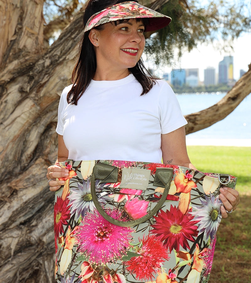 A dark haired lady wearing jeans and a white shirt and standing in front of a tree holding a large canvas floral tote bag from wild things lifestyle