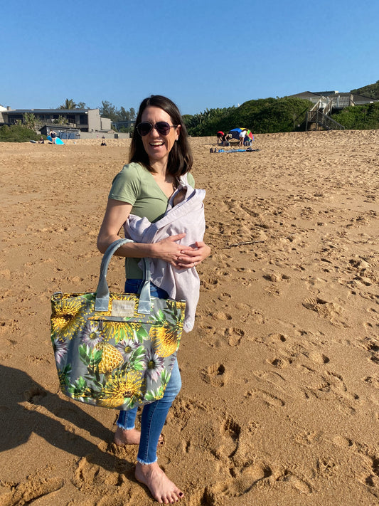 Young lady with tiny baby and large canvas floral tote bag standing on a beach