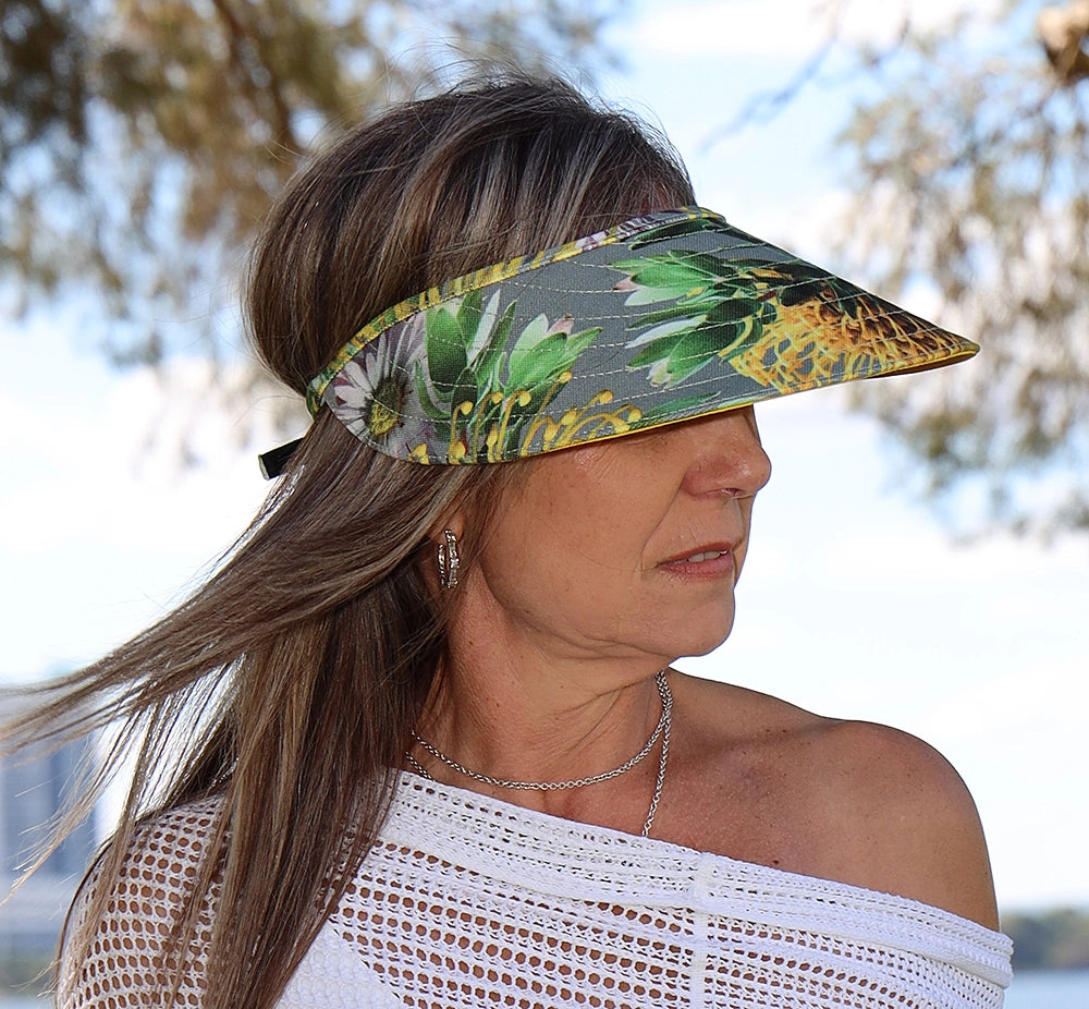 Yellow and grey floral sun visor hat worn by a woman in a white blouse. The sun visor is wide-brimmed and shades her face all around.