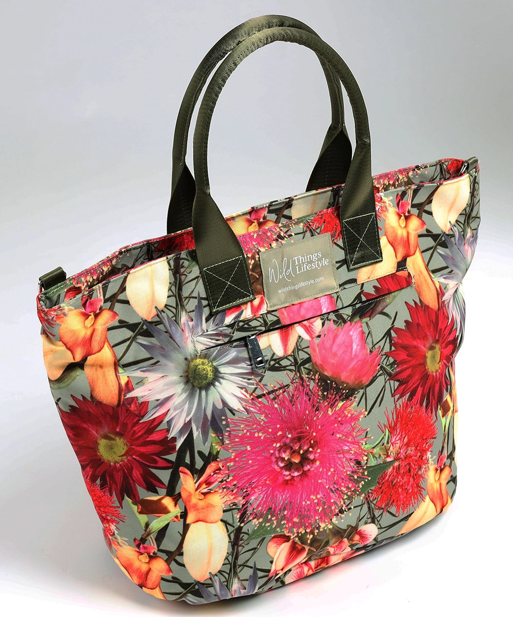 A large lifestyle bag showing the external zip pocket, green handles and bright wildflowers in pinks, reds, oranges and white on pale green canvas.